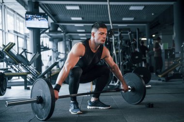 Spor kıyafetleri içindeki güçlü genç adam spor salonunda ağır toplarla egzersiz yapıyor..