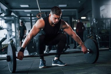 Spor kıyafetleri içindeki güçlü genç adam spor salonunda ağır toplarla egzersiz yapıyor..