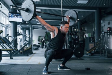 Spor kıyafetleri içindeki güçlü genç adam spor salonunda ağır toplarla egzersiz yapıyor..