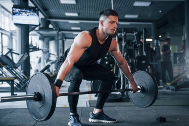 Spor kıyafetleri içindeki güçlü genç adam spor salonunda ağır toplarla egzersiz yapıyor..