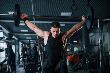 Spor kıyafetleri içindeki güçlü genç adam spor salonunda ağır toplarla egzersiz yapıyor..