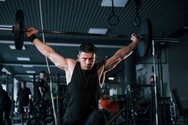 Spor kıyafetleri içindeki güçlü genç adam spor salonunda ağır toplarla egzersiz yapıyor..