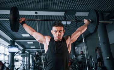 Spor kıyafetleri içindeki güçlü genç adam spor salonunda ağır toplarla egzersiz yapıyor..