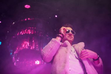 Şık elbiseli ve güneş gözlüklü bir adam gece kulübünde yürüyor..