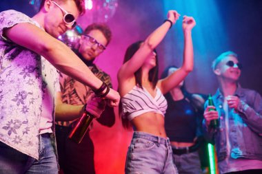 Kutlama ve şişelere alkolle vurmak. Gençler gece kulübünde renkli lazer ışıklarıyla eğleniyorlar..