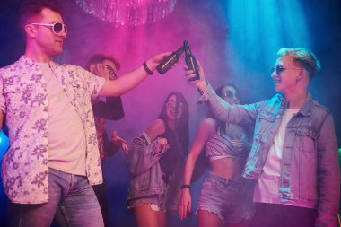 Kutlama ve şişelere alkolle vurmak. Gençler gece kulübünde renkli lazer ışıklarıyla eğleniyorlar..