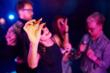 Kadının ellerine uyuşturucu hapıyla yakından bak. Gençler gece kulübünde renkli lazer ışıklarıyla eğleniyorlar..