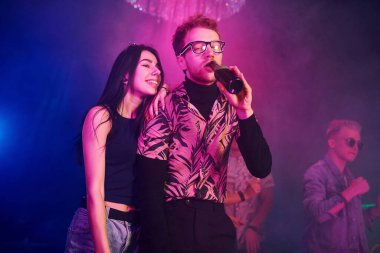 Gözlüklü adam bira içiyor. Gençler gece kulübünde renkli lazer ışıklarıyla eğleniyorlar..