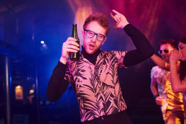 Gözlüklü adam bira içiyor. Gençler gece kulübünde renkli lazer ışıklarıyla eğleniyorlar..