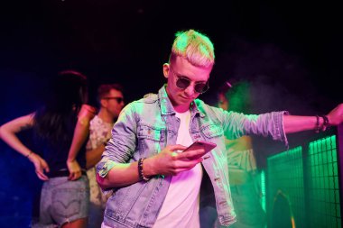 Gece kulübünde renkli lazer ışıklarıyla eğlenen insanların önünde akıllı telefonlu adam..