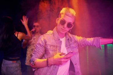 Gece kulübünde renkli lazer ışıklarıyla eğlenen insanların önünde akıllı telefonlu adam..