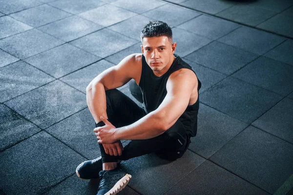 Spor elbiseli güçlü genç adam spor salonunda spor yapıyor, oturuyor ve mola veriyor..