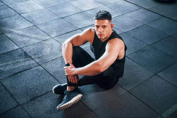 Spor elbiseli güçlü genç adam spor salonunda spor yapıyor, oturuyor ve mola veriyor..