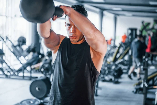 Spor kıyafetleri içindeki güçlü genç adam spor salonunda ağır toplarla egzersiz yapıyor..