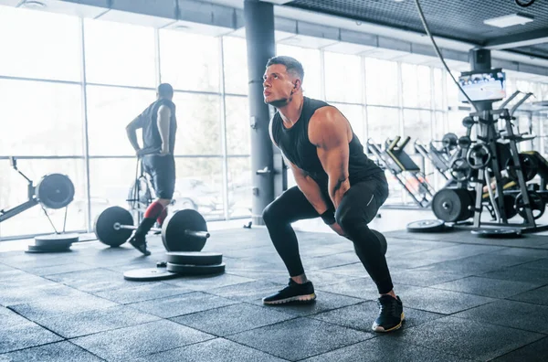 Spor kıyafetleri içindeki güçlü genç adam spor salonunda ağır toplarla egzersiz yapıyor..