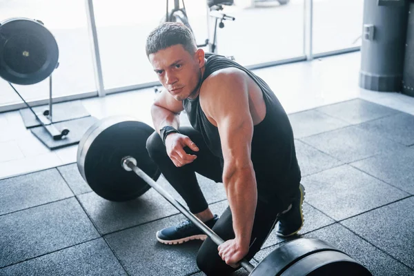 Spor kıyafetleri içindeki güçlü genç adam spor salonunda ağır toplarla egzersiz yapıyor..