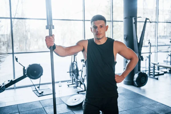 Spor elbiseli güçlü genç adam spor salonunda duruyor..