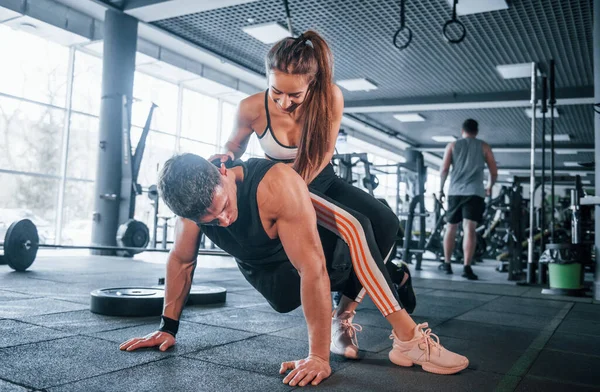 Kadın şınav çeken adamın üstüne oturur. Spor salonunda birlikte egzersiz yapan genç insanlar..