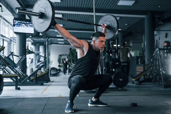 Spor kıyafetleri içindeki güçlü genç adam spor salonunda ağır toplarla egzersiz yapıyor..