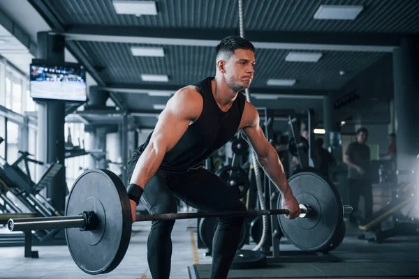 Spor kıyafetleri içindeki güçlü genç adam spor salonunda ağır toplarla egzersiz yapıyor..