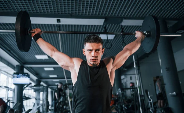 Spor kıyafetleri içindeki güçlü genç adam spor salonunda ağır toplarla egzersiz yapıyor..