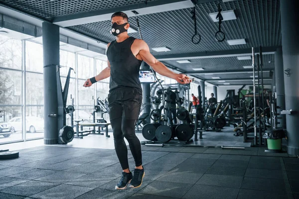 Spor elbiseli ve maskeli güçlü genç adam spor salonunda ip atlamakla egzersiz yapıyor..