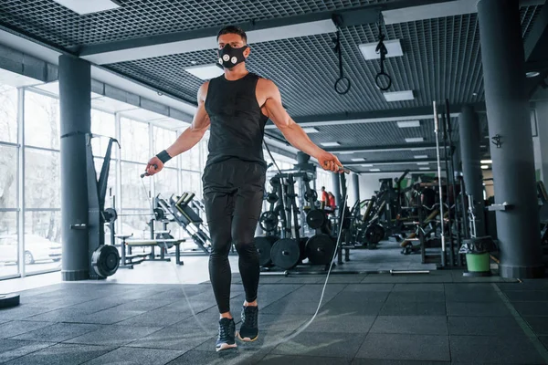 Spor elbiseli ve maskeli güçlü genç adam spor salonunda ip atlamakla egzersiz yapıyor..