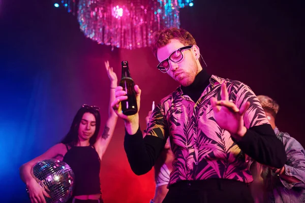 Gözlüklü adam bira içiyor. Gençler gece kulübünde renkli lazer ışıklarıyla eğleniyorlar..