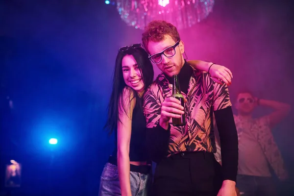 Guy in glasses drinks beer. Young people is having fun in night club with colorful laser lights.