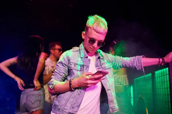 Gece kulübünde renkli lazer ışıklarıyla eğlenen insanların önünde akıllı telefonlu adam..