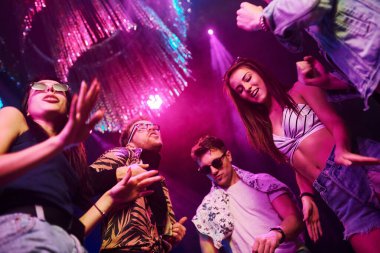 Gece kulübünde renkli lazer ışıklarıyla eğlenen gençlerin manzarası.