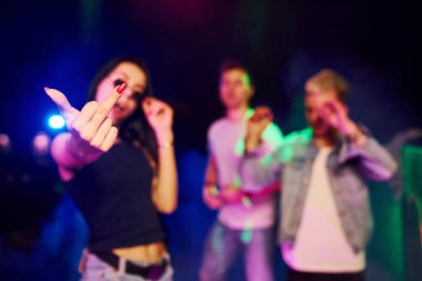 Gözlüklü kadın orta parmak gösteriyor. Gençler gece kulübünde renkli lazer ışıklarıyla eğleniyorlar..