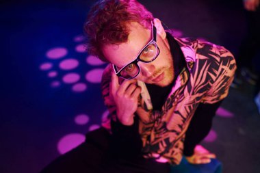 Gözlüklü genç adam, gece kulübünde pembe ışıklı eğleniyor..