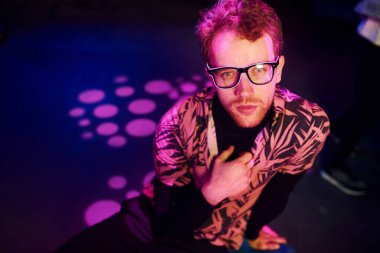 Gözlüklü genç adam, gece kulübünde pembe ışıklı eğleniyor..