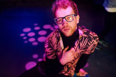 Gözlüklü genç adam, gece kulübünde pembe ışıklı eğleniyor..