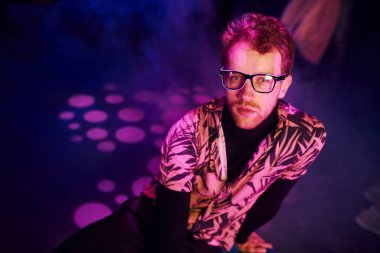 Gözlüklü genç adam, gece kulübünde pembe ışıklı eğleniyor..