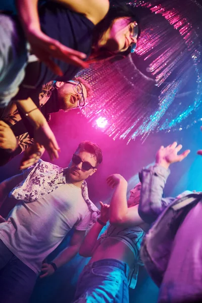 Gece kulübünde renkli lazer ışıklarıyla eğlenen gençlerin manzarası.