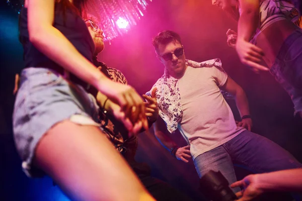 Gece kulübünde renkli lazer ışıklarıyla eğlenen gençlerin manzarası.