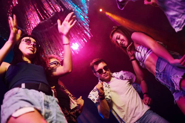 Gece kulübünde renkli lazer ışıklarıyla eğlenen gençlerin manzarası.