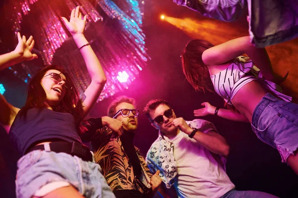 Gece kulübünde renkli lazer ışıklarıyla eğlenen gençlerin manzarası.