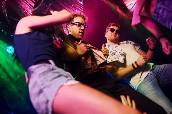 Gece kulübünde renkli lazer ışıklarıyla eğlenen gençlerin manzarası.