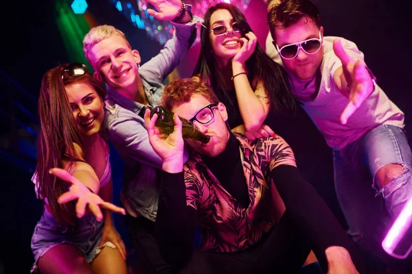 Çılgına dönüp kameraya poz vermek. Gençler gece kulübünde renkli lazer ışıklarıyla eğleniyorlar..