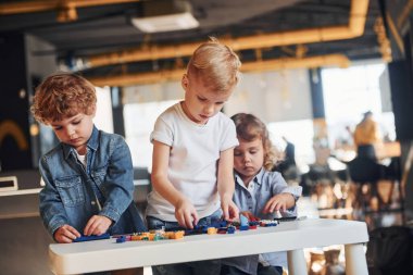 Küçük arkadaşlar oyun odasında inşaat oyuncaklarıyla eğleniyor. Anaokulu eğitim oyunları.