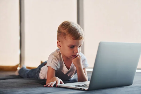 stock image Little boy in casual clothes lying down on the ground with laptop.