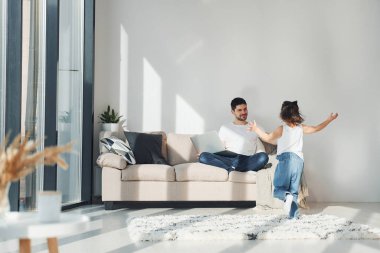 Happy father with his daughter spending free time with laptop at home together.