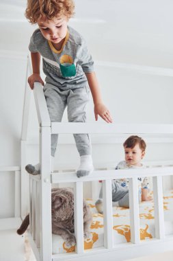 İki küçük çocuk dinleniyor ve yatak odasında birlikte eğleniyorlar. Kedi oturuyor..
