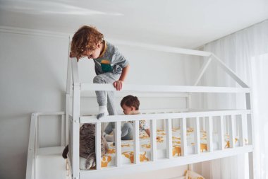 İki küçük çocuk dinleniyor ve yatak odasında birlikte eğleniyorlar. Onların yanında oturan kedi..