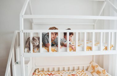 İki küçük çocuk dinleniyor ve yatak odasında birlikte eğleniyorlar. Onların yanında oturan kedi..