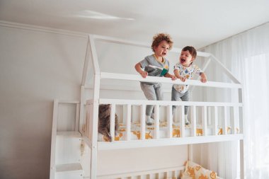 İki küçük çocuk dinleniyor ve yatak odasında birlikte eğleniyorlar. Onların yanında oturan kedi..