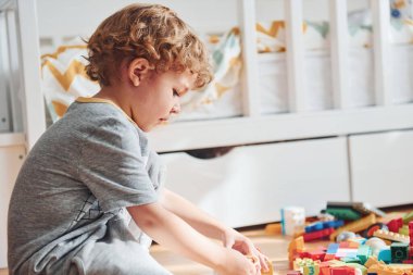 Cute little boy sitting and have fun indoors in the bedroom with plastic construction set.